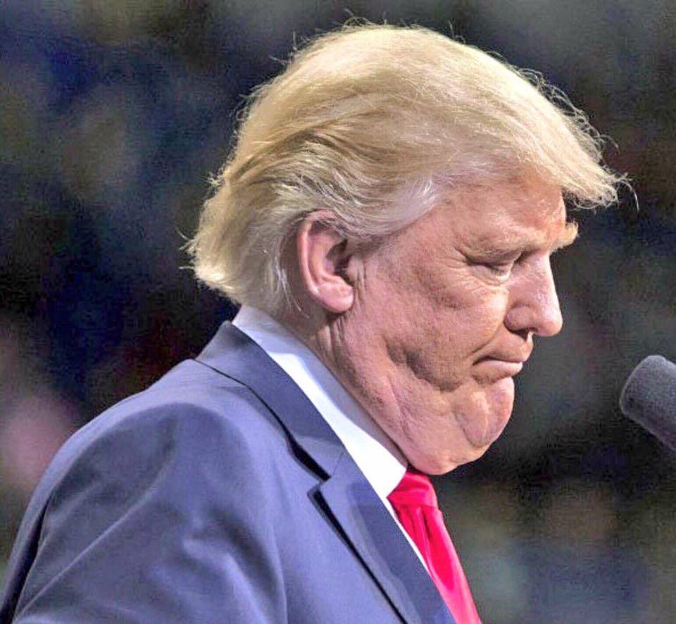 Donald Trump looking downward, seen from the side, in a blue suit and red tie